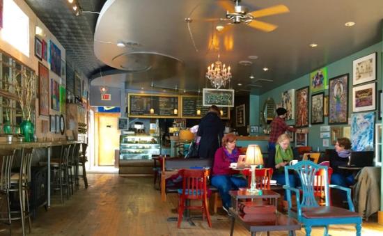 A colorful coffee shop with art on the walls and people lounging and drinking coffee
