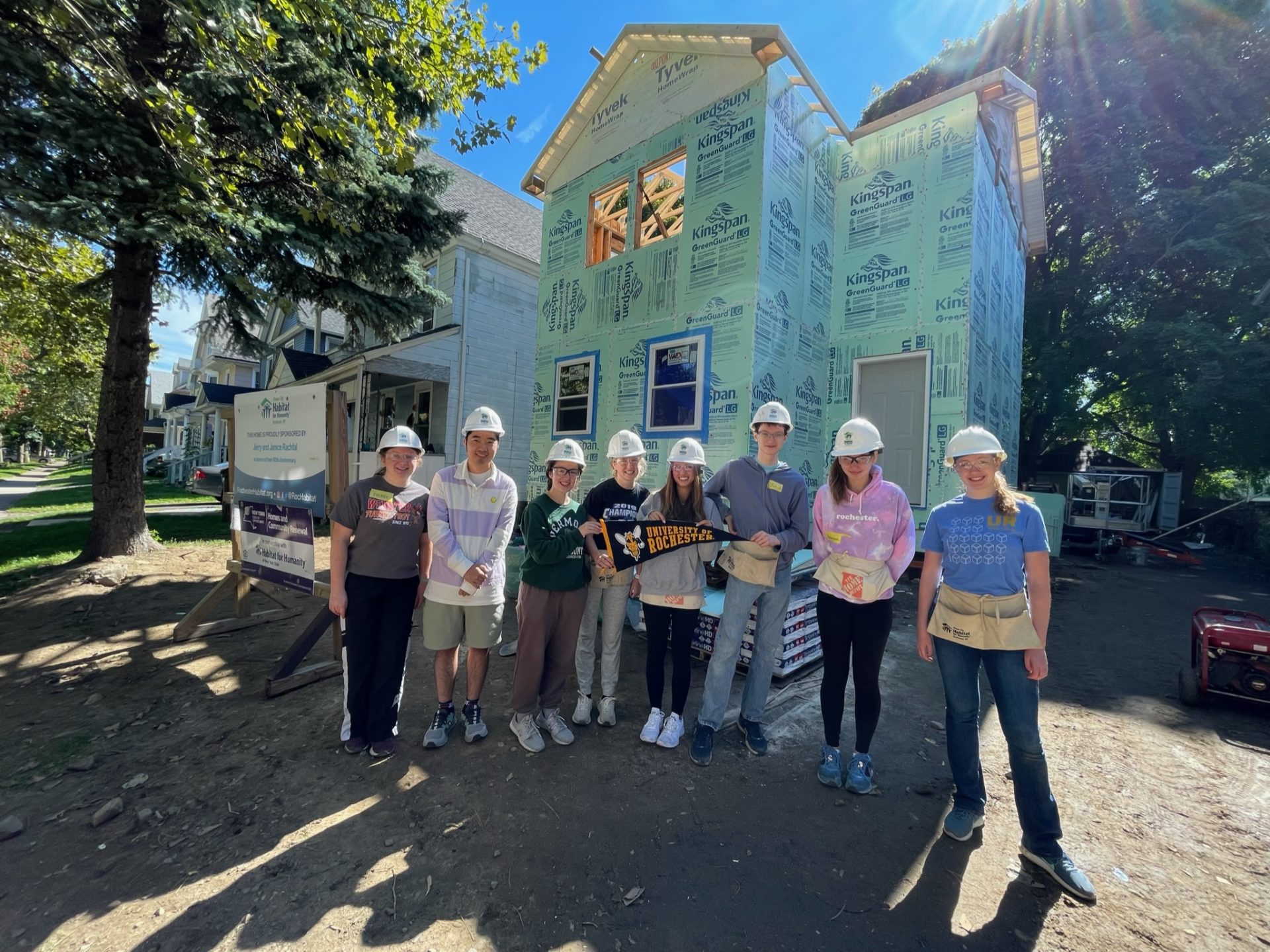 Group of 8 UR Habitat volunteers in front of a partially constructed house.