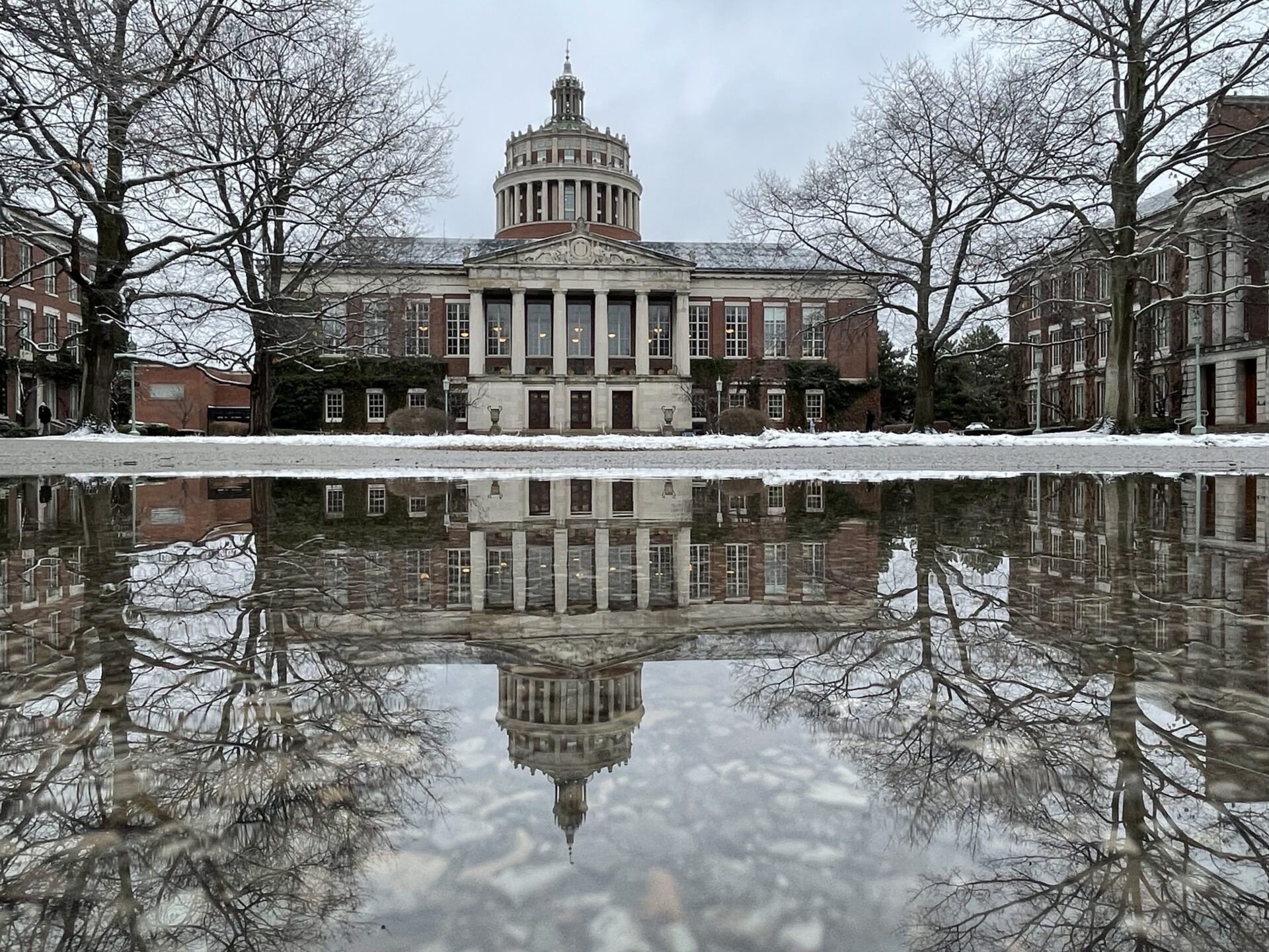 A reflection of Rush Rhees library on a winter day framed by leafless trees.