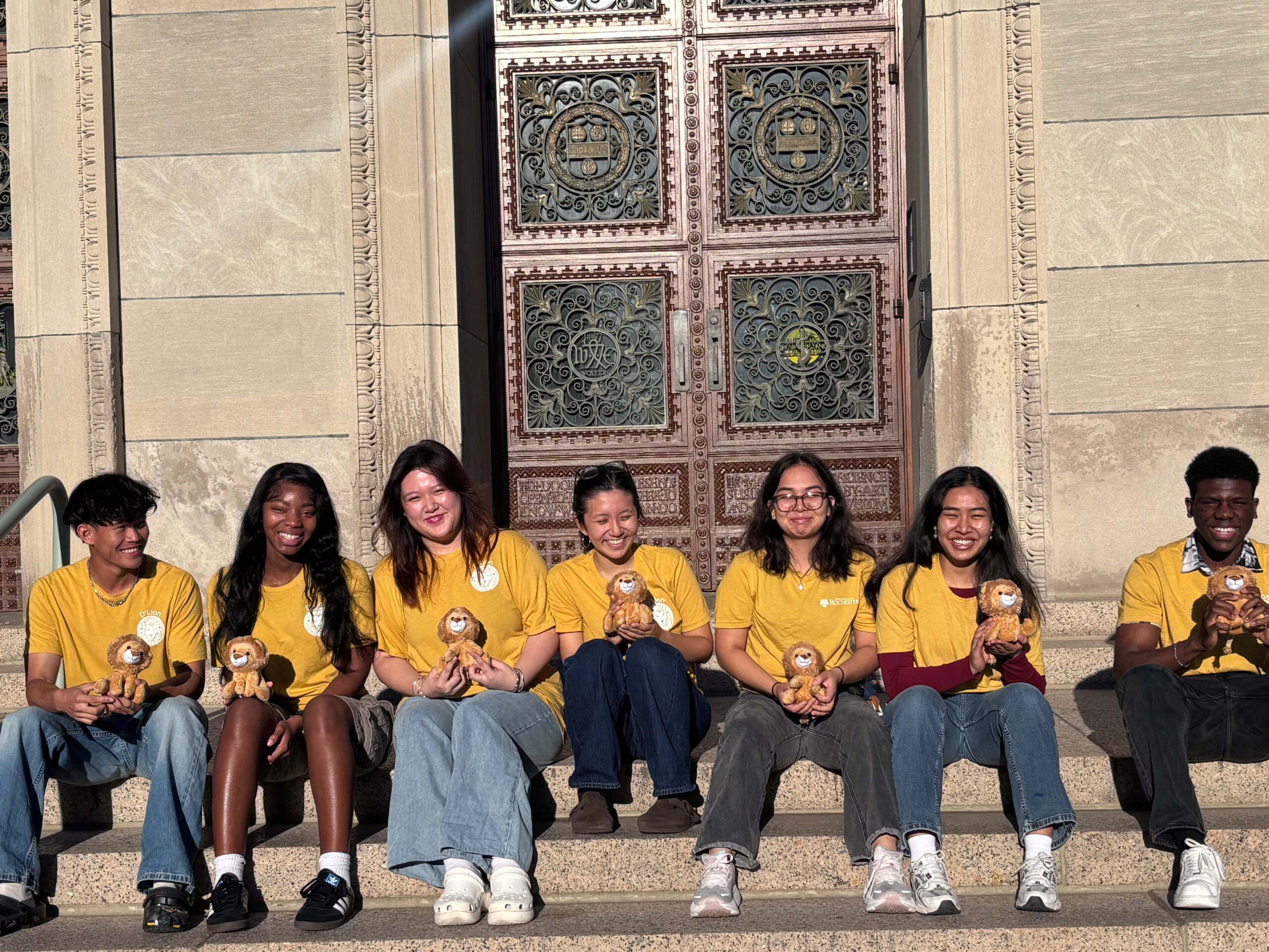 The 2025-2026 D’Lion E-Board members pose for a photo in front of a door to Rush Rhees Library.