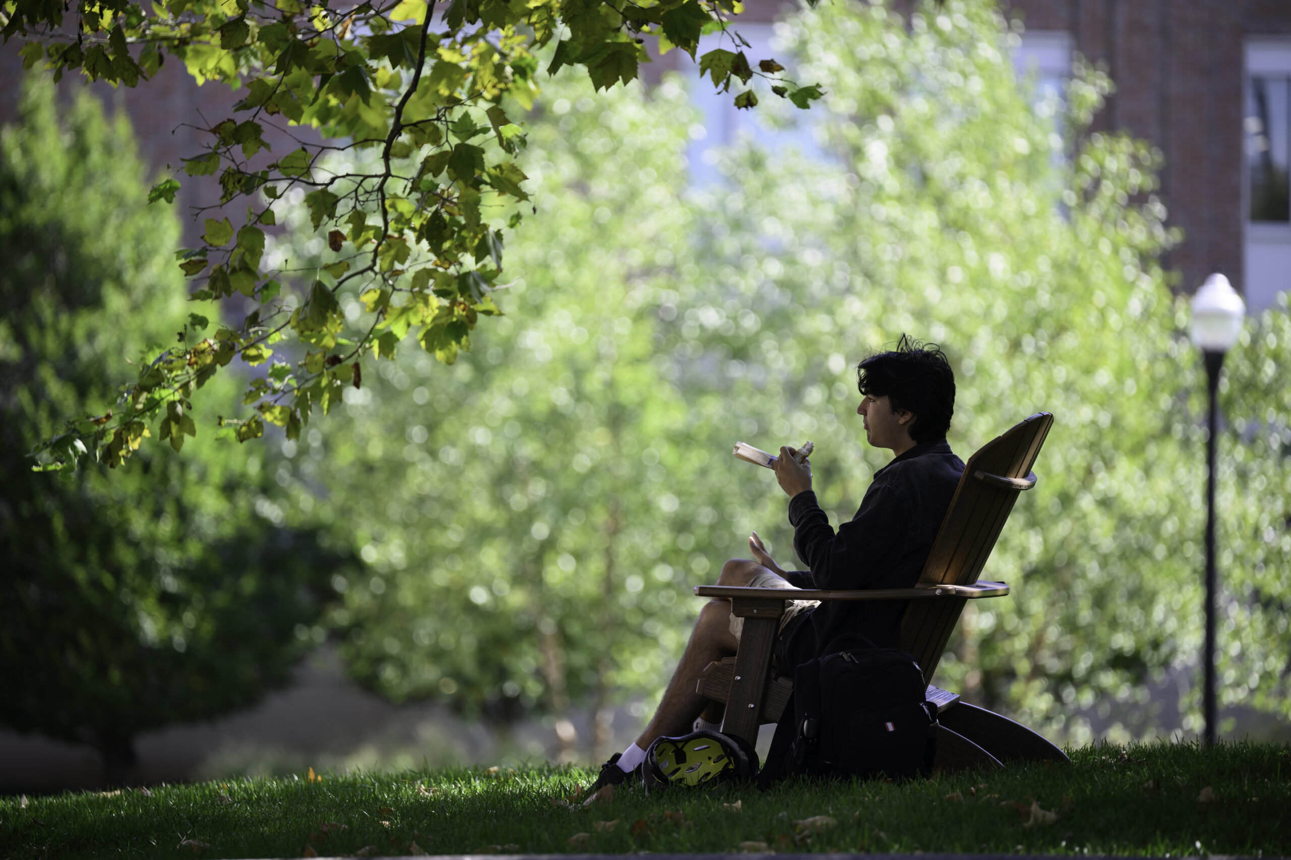 A student sits in an Adirondack chair in Hajim Quad.