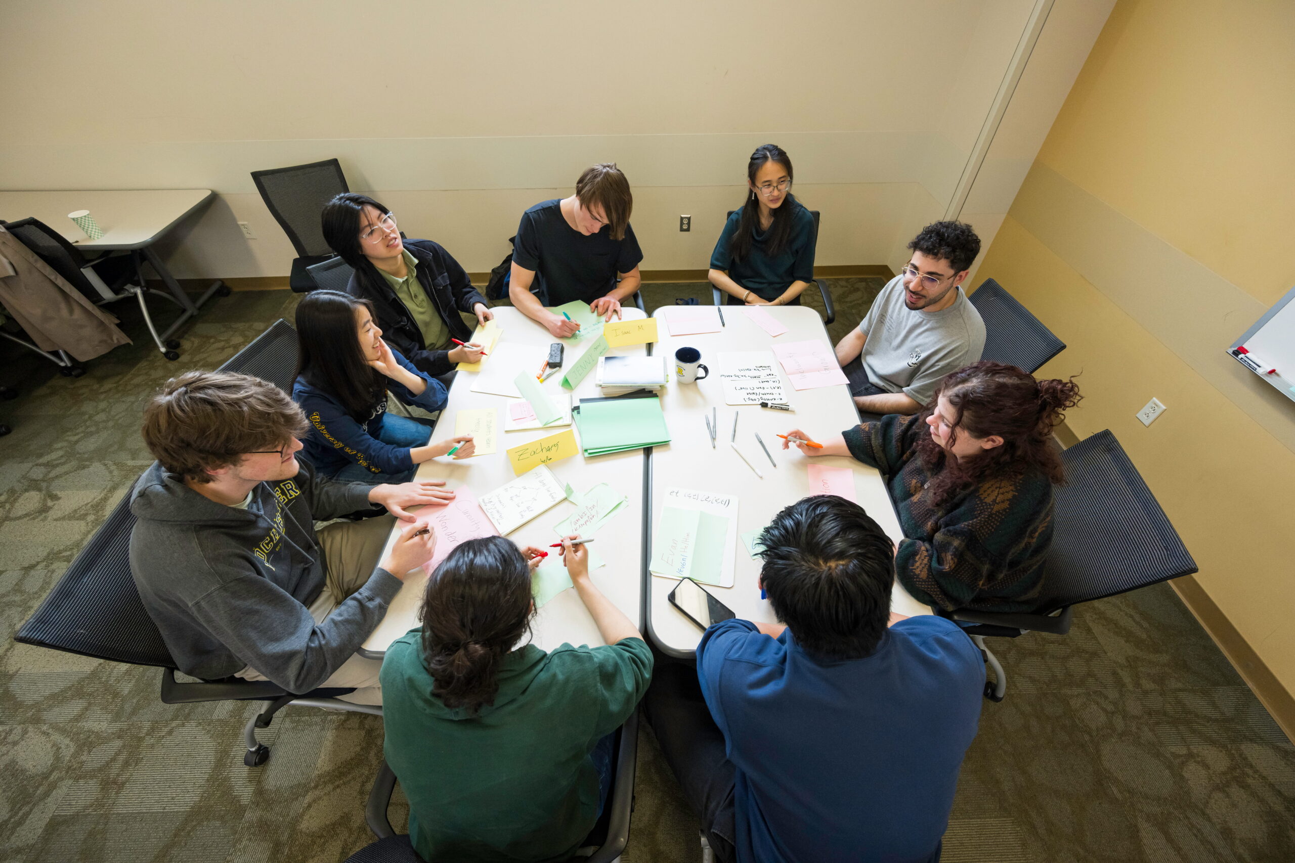 Nine students gather around a large table in the Learning Center at URochester.
