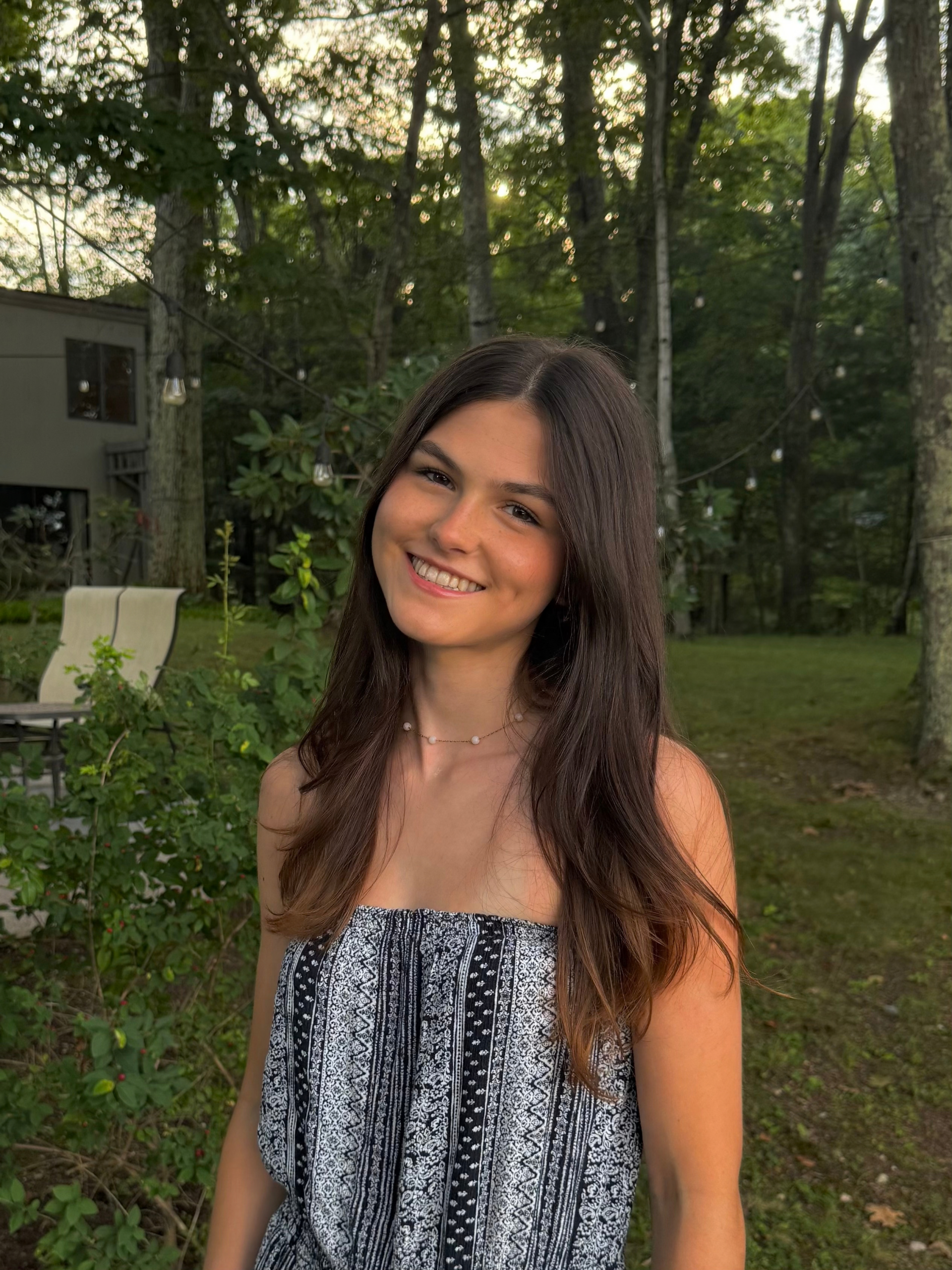 A URochester student with long dark hair wears a blue patterned tube top in front of a green, tree-filled area.