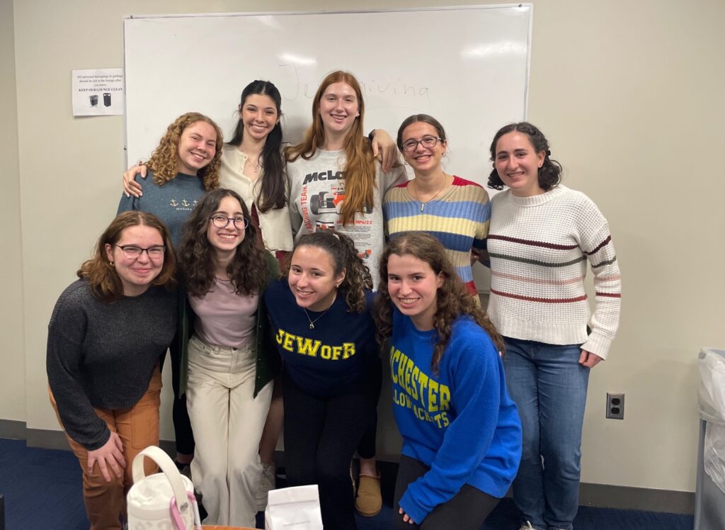 Nine female student pose for a photo in front of a white board in classroom. 