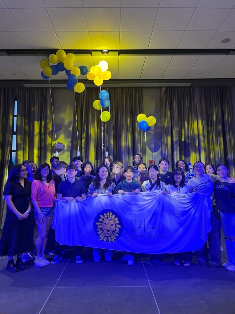 A large group of students hold up a D'Lion Organization banner.