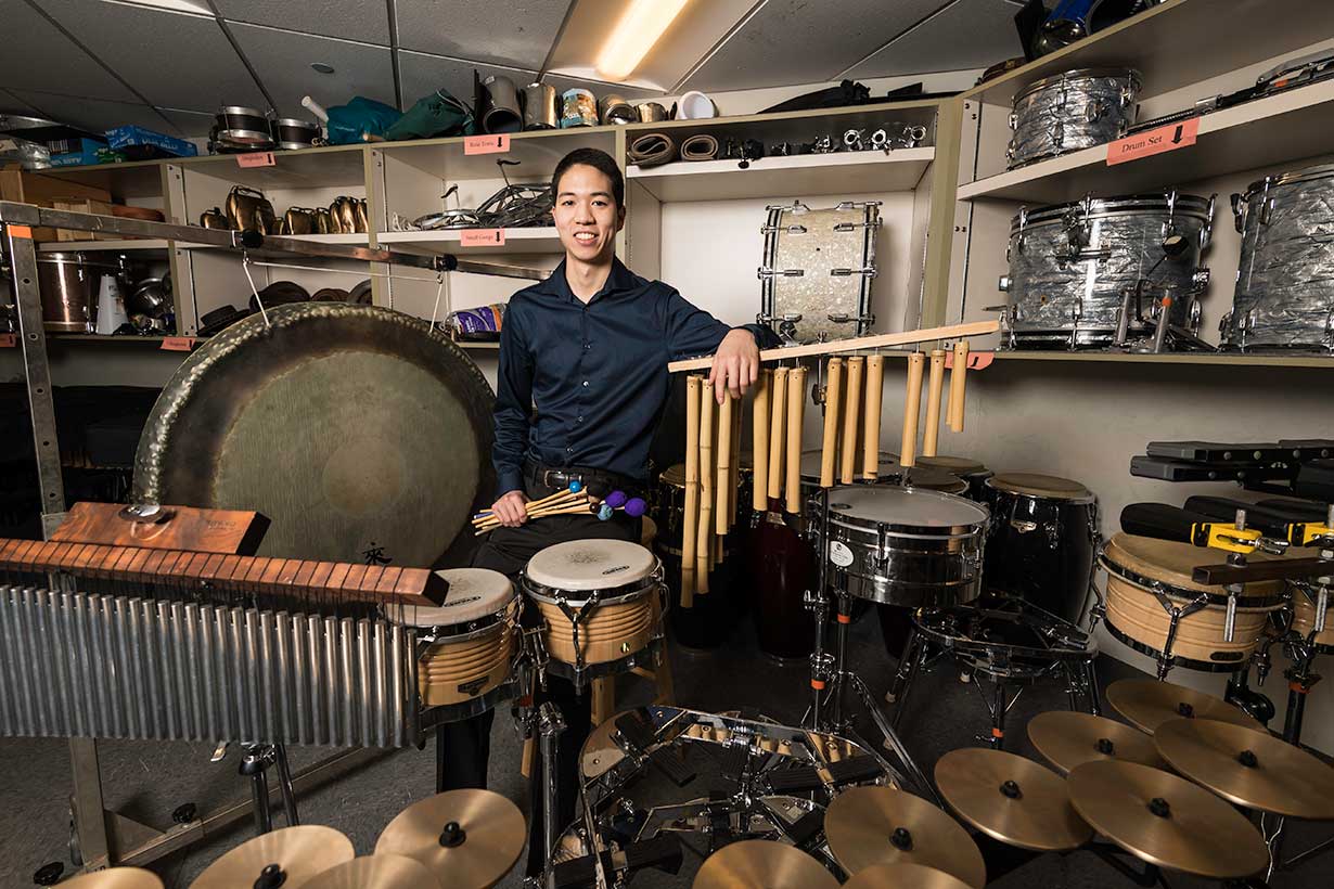 A dual degree student standing with percussion instruments.