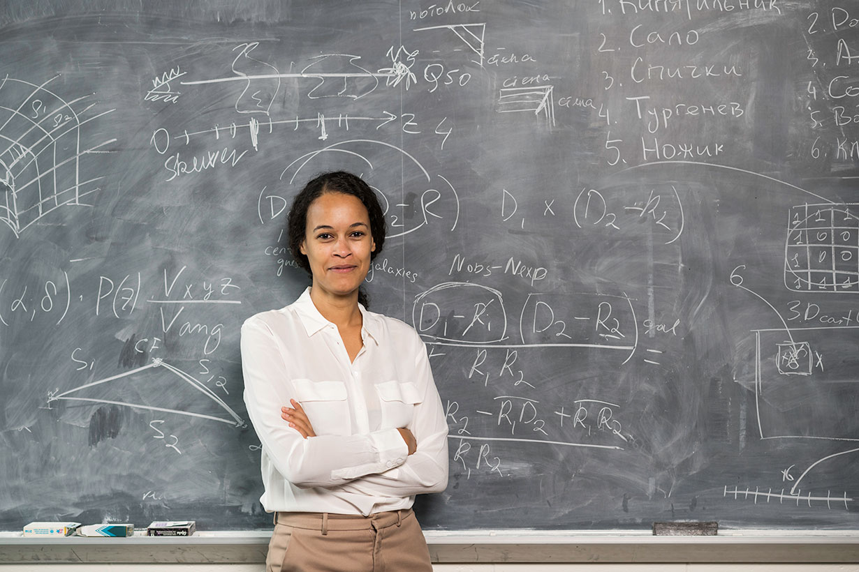 An instructor standing in front of a blackboard with equations.