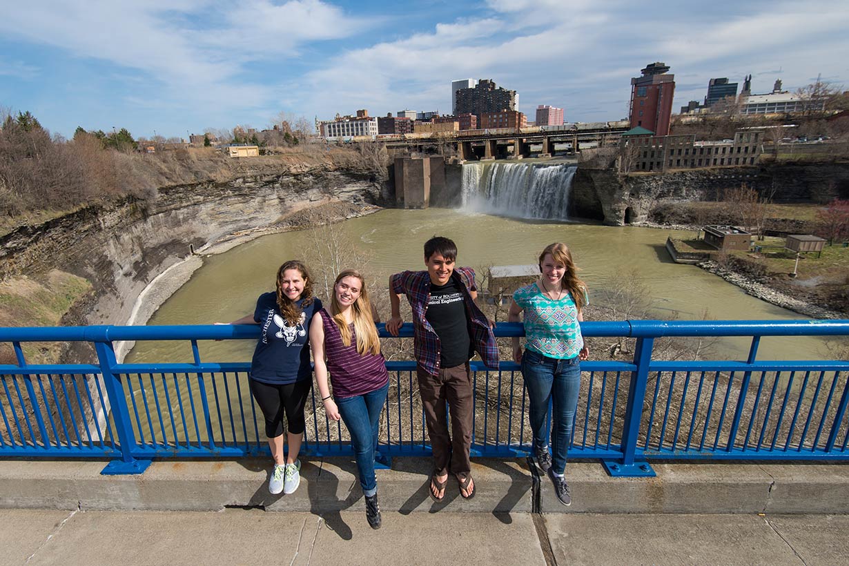 Four students standing on the Genesee River Bridge with High Falls in the background.