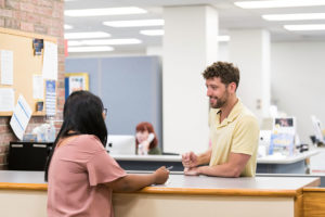 An advisor speaking with a student at a counter.