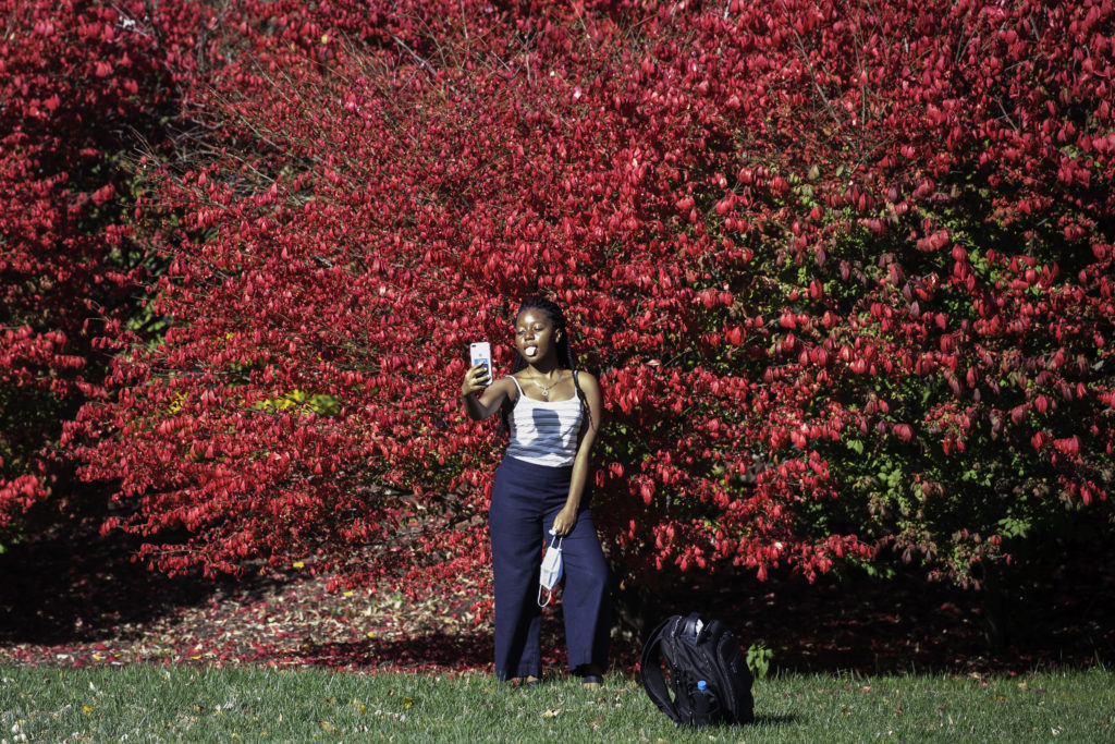 A student poses for a selfie as leaves change color.
