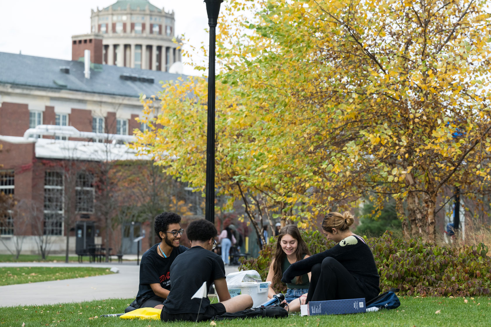 University of Rochester students sitting on the grass in front of a building, engaged in conversation and study.