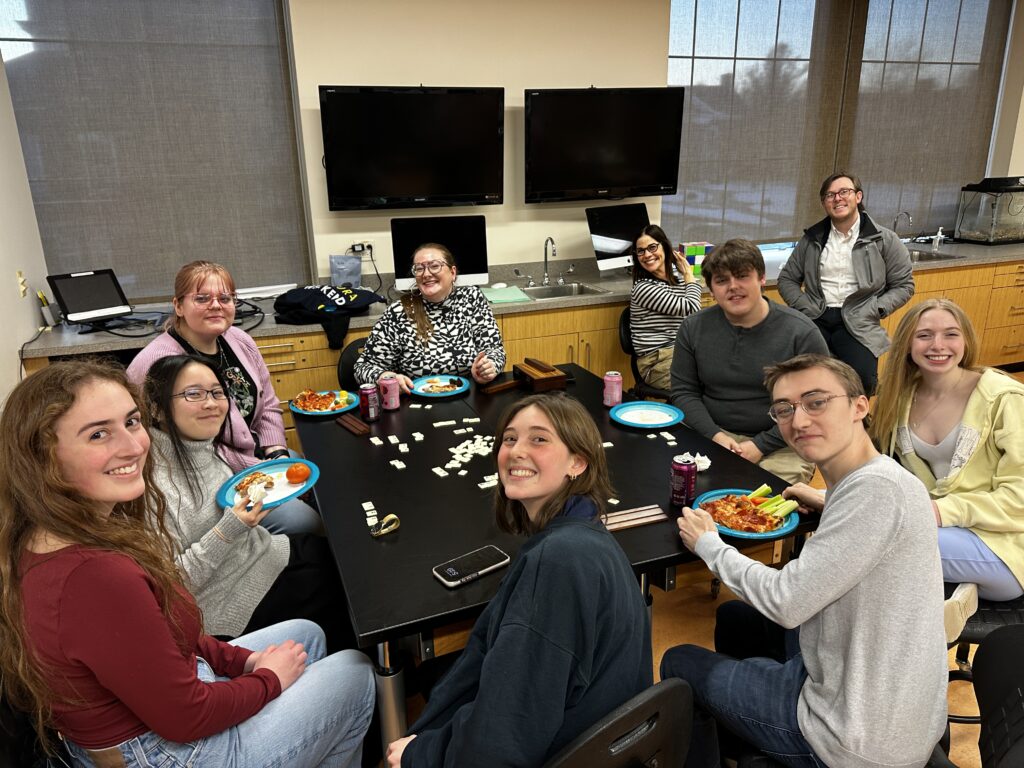 URochester students sit arounds a black table and enjoy pizza and soda.