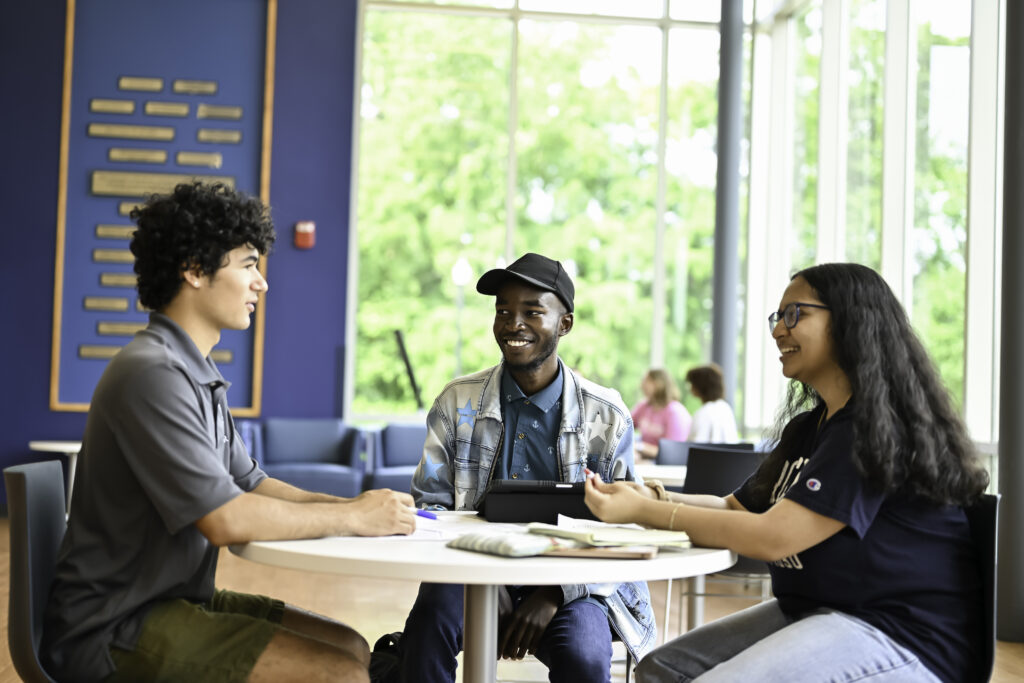 Three URochester students sit around a table chatting.