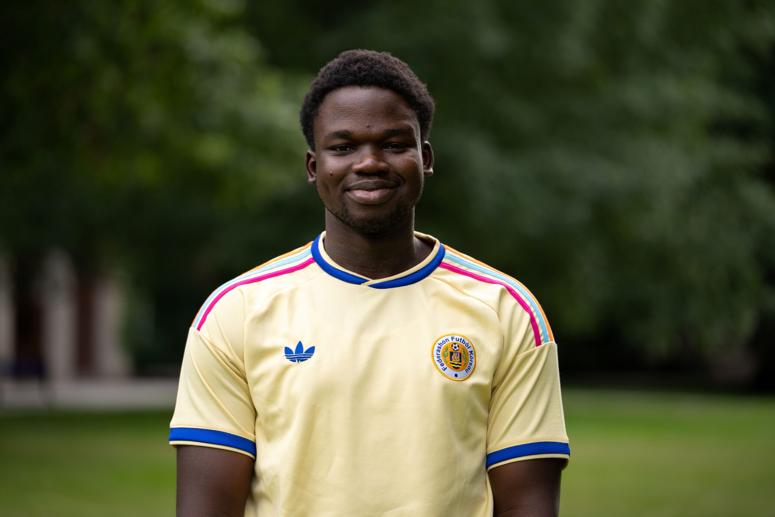 A student with short, dark hair wears a light yellow jersey on Eastman Quad.