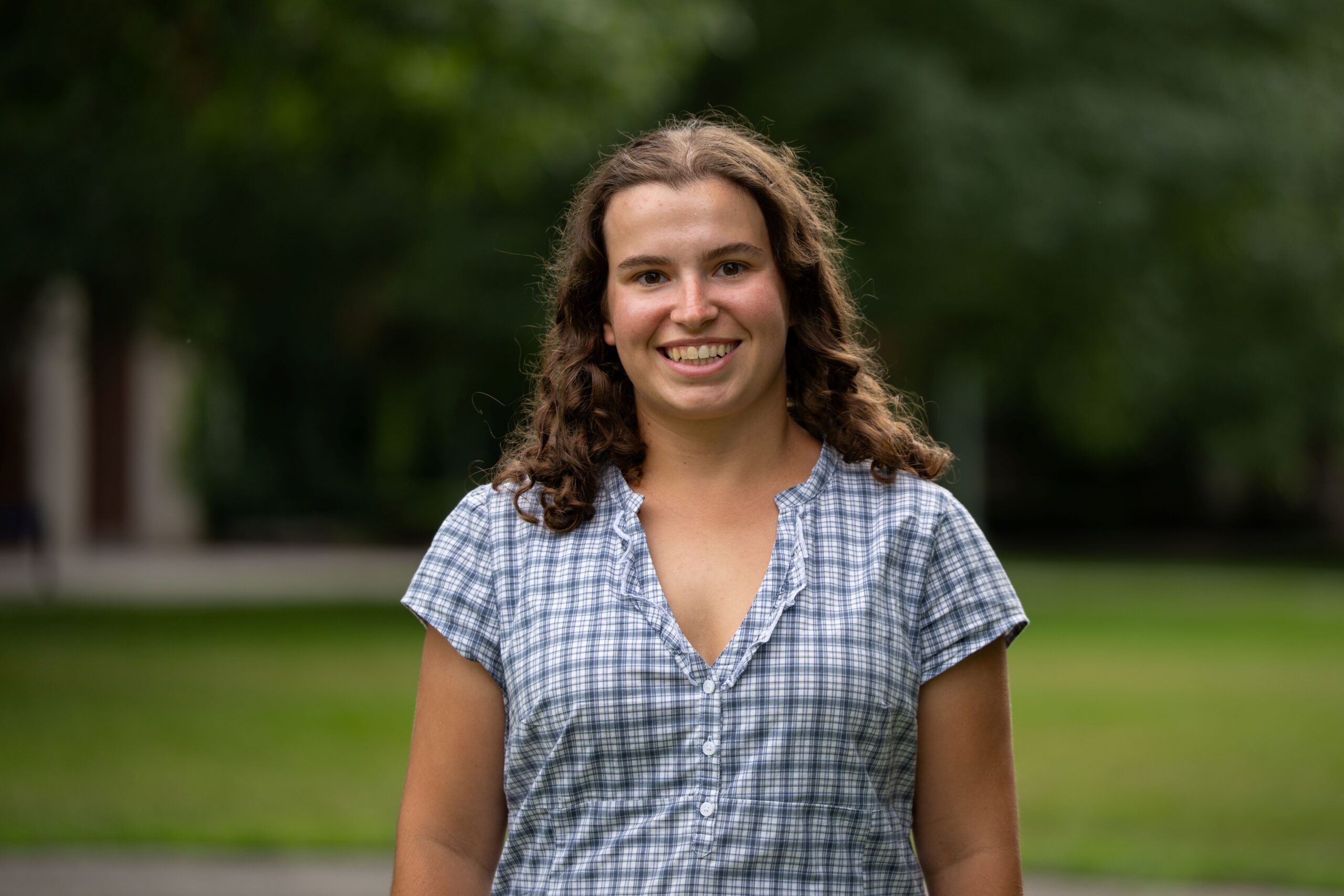 A student with long, curly brown hair wears a blue plaid blouse on Eastman Quad.
