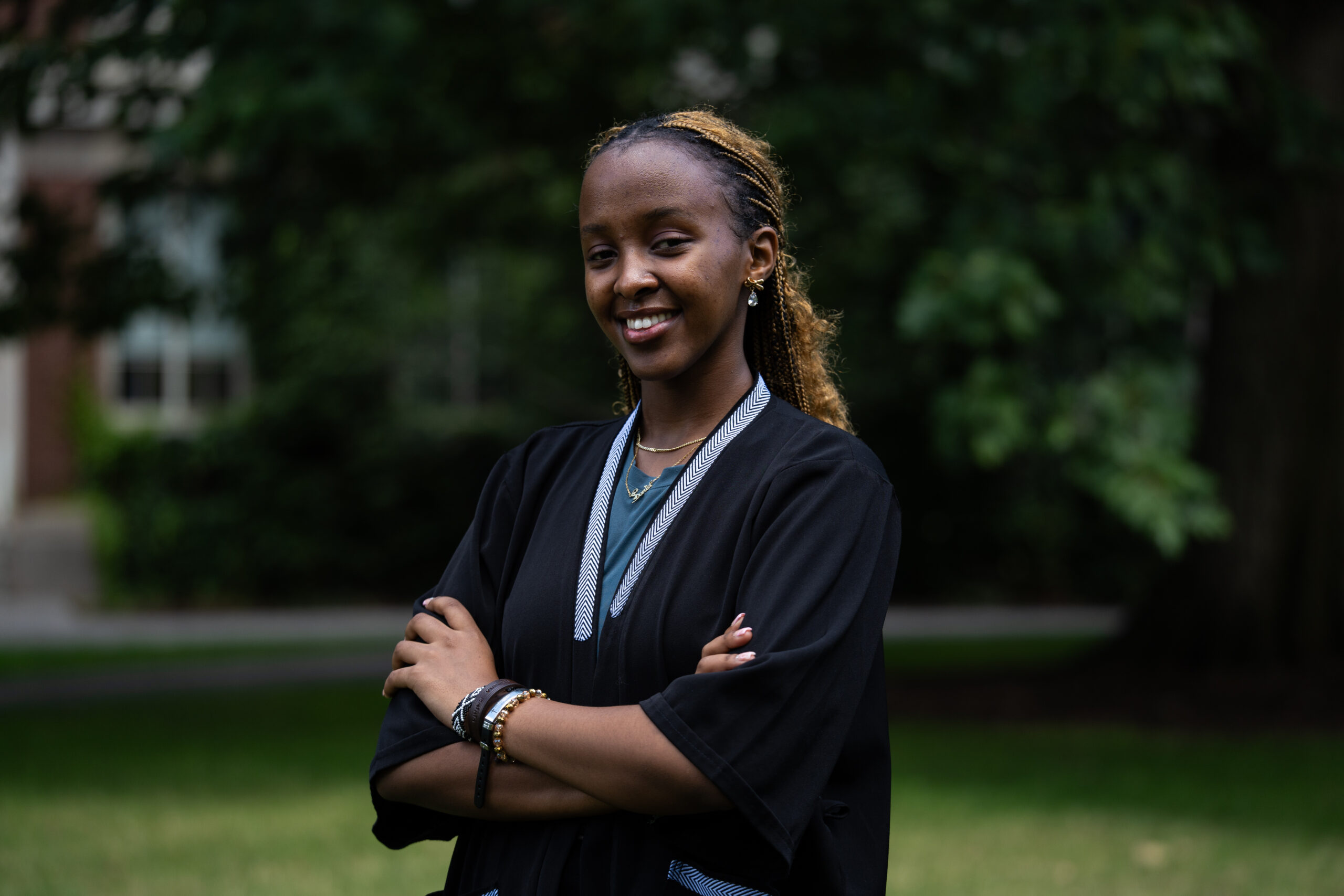 A student stands in a black top stands on Eastman Quad with her arms crossed.